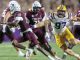 LSU defender wearing number 97 in white and gold chases a Texas A&M quarterback in maroon as he runs with the ball during a college football game.