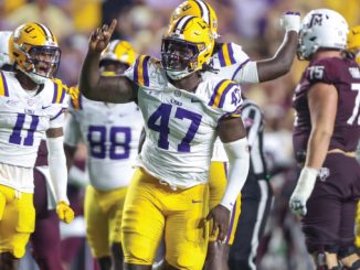 LSU football players in white and purple-yellow uniforms celebrate on the field, center wearing #47 raising a fist in victory.