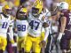 LSU football players in white and purple-yellow uniforms celebrate on the field, center wearing #47 raising a fist in victory.