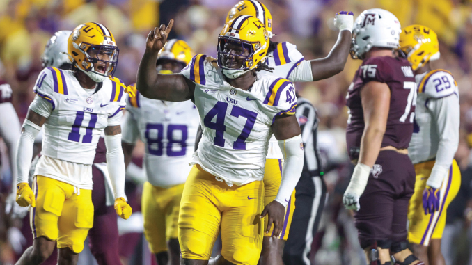 LSU football players in white and purple-yellow uniforms celebrate on the field, center wearing #47 raising a fist in victory.