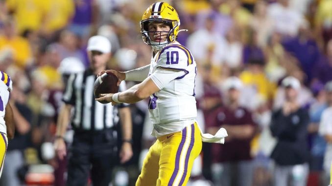 Louisiana State University quarterback in white and gold uniform holding a football as he scans the field during a game.