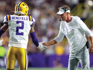 LSU Tigers player Benefield (#2) in white jersey shakes hands with a coach on the sideline during a game.