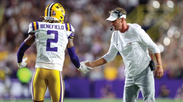 LSU Tigers player Benefield (#2) in white jersey shakes hands with a coach on the sideline during a game.