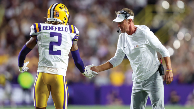 LSU Tigers player Benefield (#2) in white jersey shakes hands with a coach on the sideline during a game.