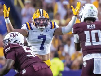 LSU quarterback #7 raises arms in celebration as Texas A&M defenders close in during a football game.