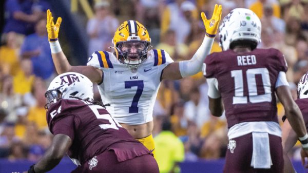 LSU quarterback #7 raises arms in celebration as Texas A&M defenders close in during a football game.
