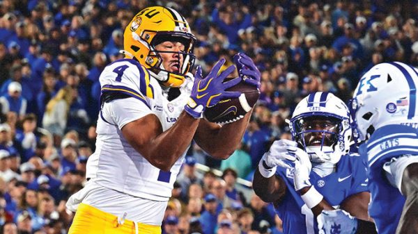 LSU wide receiver in white and yellow reaches to catch a pass as Kentucky defenders close in.