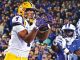 LSU wide receiver in white and yellow reaches to catch a pass as Kentucky defenders close in.