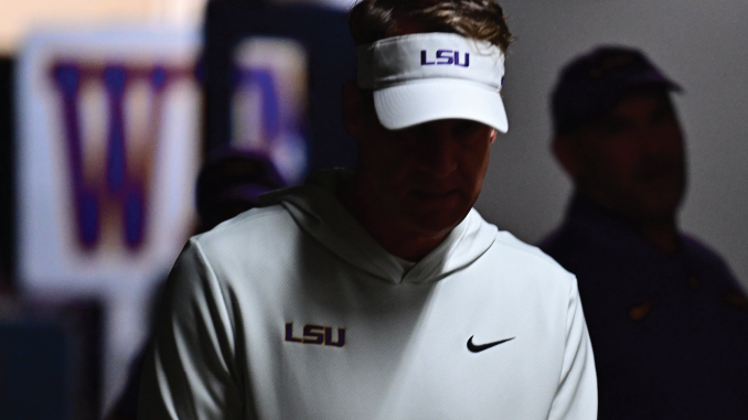 Person wearing a white LSU visor and hoodie with a Nike swoosh, head bowed in a dimly lit setting.