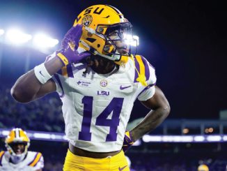 LSU football player wearing number 14 saluting with his right hand during a night game on the field.