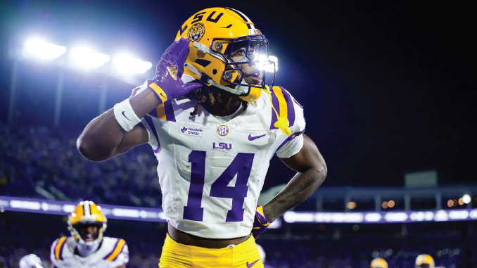 LSU football player wearing number 14 saluting with his right hand during a night game on the field.