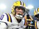 LSU quarterback grins during a celebration with teammates on the field, wearing a yellow helmet with LSU logo.