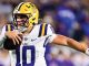LSU quarterback wearing number 10 runs with a football in a white and purple uniform during a game.
