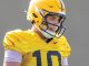 Football player wearing a yellow jersey (#10) and helmet, looking down in concentration on the field.