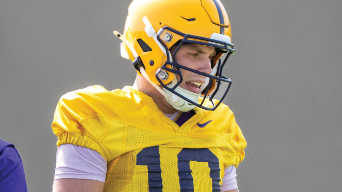 Football player wearing a yellow jersey (#10) and helmet, looking down in concentration on the field.