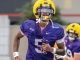 A college football player in a purple jersey with the number 5 and a yellow helmet runs on the field, with another purple-jersey teammate in the background.