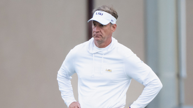 Man wearing a white LSU visor and hoodie stands with hands on hips, looking focused outside.