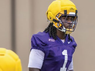 Young football player in purple jersey with #1, wearing a yellow helmet, during practice on a field.