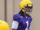 Young football player in purple jersey with #1, wearing a yellow helmet, during practice on a field.