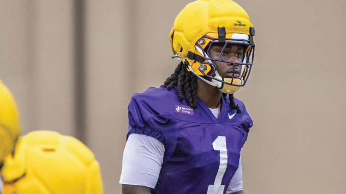 Young football player in purple jersey with #1, wearing a yellow helmet, during practice on a field.
