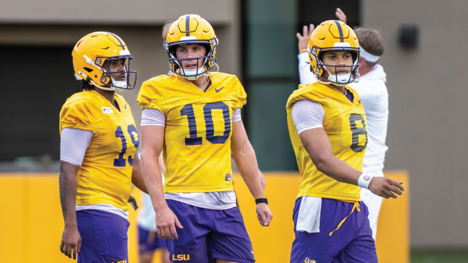 Three LSU football players in yellow practice uniforms stand on a field, center #10 flanked by teammates #15 and #8.