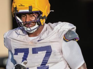 Football player in a white jersey with the number 77 and a yellow helmet on the field.