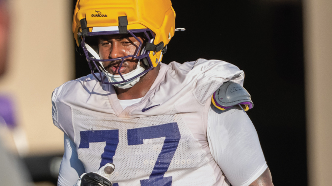 Football player in a white jersey with the number 77 and a yellow helmet on the field.