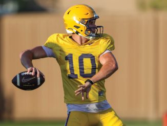 Quarterback in yellow uniform (#10) about to throw a football during practice on a grassy field.