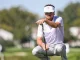 Golfer in a white visor crouching with a putter on a sunny golf course.