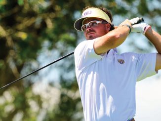 Golfer wearing an LSU visor and white polo mid-swing on a sunny golf course.