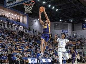 Basketball player in blue and gold (No. 99) dunks the ball over a defender while a full arena watches.