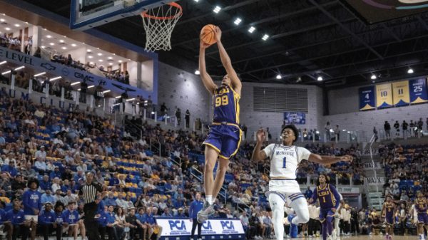 Basketball player in blue and gold (No. 99) dunks the ball over a defender while a full arena watches.