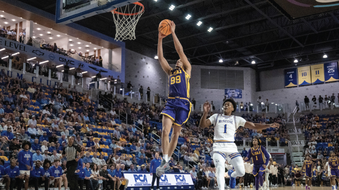 Basketball player in blue and gold (No. 99) dunks the ball over a defender while a full arena watches.