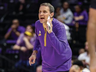 Basketball coach in a purple uniform shouting instructions on the sideline during a game.