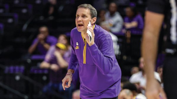 Basketball coach in a purple uniform shouting instructions on the sideline during a game.