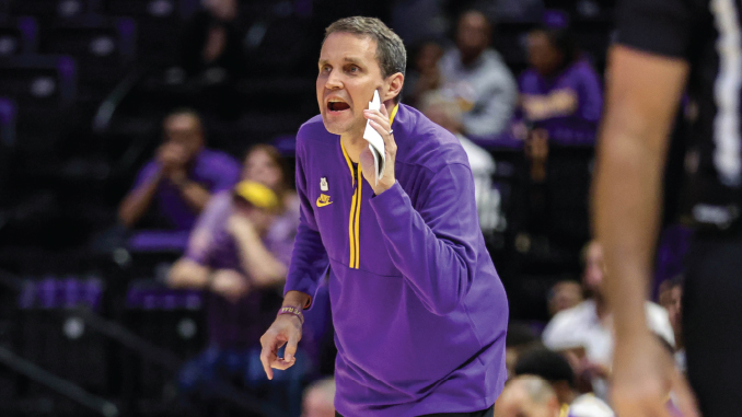 Basketball coach in a purple uniform shouting instructions on the sideline during a game.