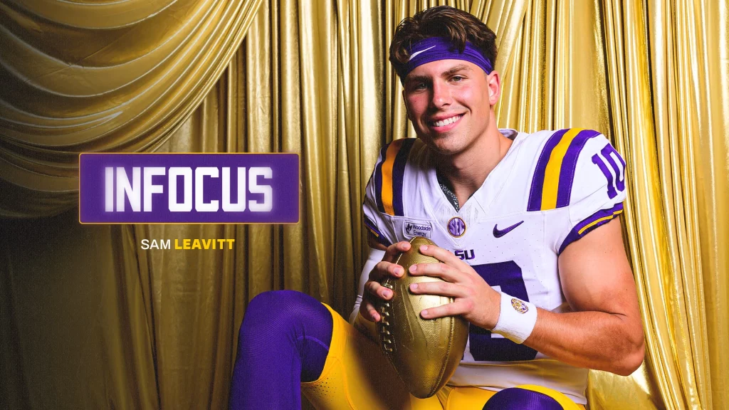 LSUSamLeavitt | TigerRag.com Portrait of Sam Leavitt in LSU-style purple and gold uniform, smiling while holding a gold football against a shiny gold curtain backdrop