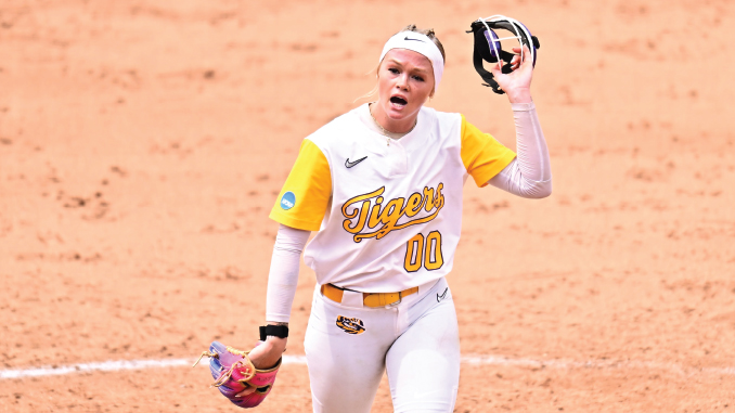 Softball player in a white and gold Tigers uniform (number 00) raises her glove during a game on the orange dirt infield on the mound.