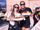 Two smiling women in sunglasses hold plates of food at an outdoor campus event, with a brick building and an LSU banner in the background.