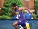 LSU sprinter in purple uniform running on a track during a race, crowd in the background.