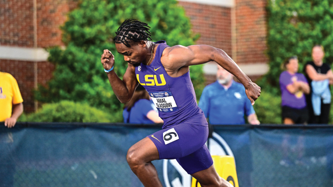 LSU sprinter in purple uniform running on a track during a race, crowd in the background.