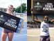 Two track athletes holding a large '2026 Ticket Punched' banner, celebrating qualification.