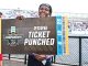 Smiling athlete holds a large mock ticket reading '2026 TICKET PUNCHED' at a track and field championships event.
