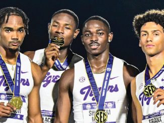 Four male college sprinters in white-and-purple Tigers uniforms pose with gold medals around their necks after an SEC championship, one biting a medal in the center-left.