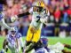 LSU player in white jersey with yellow pants runs with the ball while defenders in purple chase from behind on a college football field.