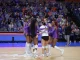 Group of female volleyball players in purple uniforms hug in a huddle on the court during a match you can see the crowd in the stands behind them.