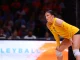 Female volleyball player in a yellow LSU jersey crouches on the court, ready to receive the ball as spectators watch in the background.