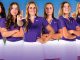 Six female athletes in matching purple tops and white skirts stand in a row, posing confidently as a team photo.