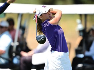 Female golfer in a purple shirt and white skirt mid-swing on a golf course, with spectators and golf carts in the background.