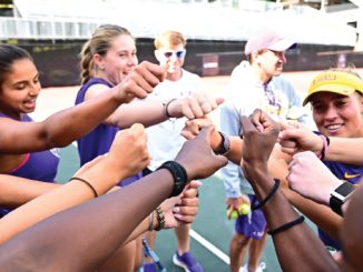 Group of diverse young athletes in a circle joining their fists for a team cheer on a track field.